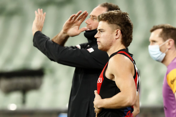 Essendon coach Ben Rutten signals from the bench that the Bombers have used all their interchanges, while medical sub Brayden Ham looks on.