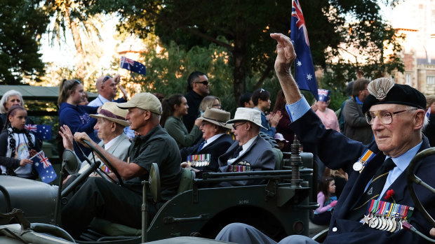 Korean War veterans wave to parade attendees as they drive down St Georges Terrace in a historical car.