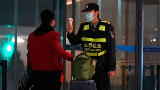 An airport staff member uses a temperature gun to check people leaving Wuhan Tianhe International Airport.