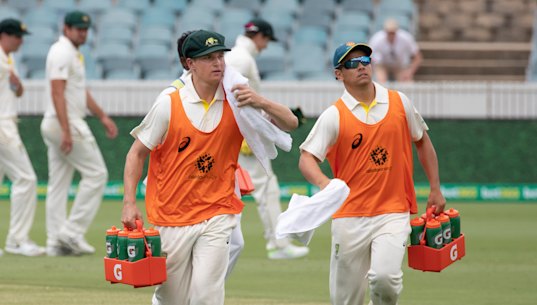 Substitute fielders Tom Vane-Tempest and Dan Leerdam run drinks out to the Australian cricket team.