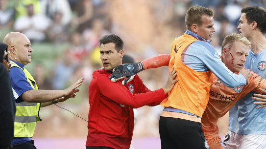 A bloodied Tom Glover is escorted from the pitch by teammates.