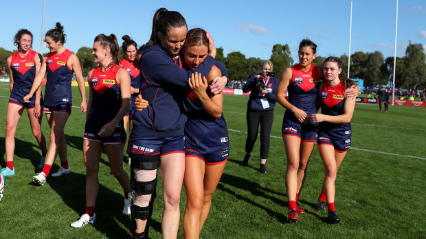 Daisy Pearce, wearing a leg brace, hugs teammate Eliza McNamara after the Demons defeated the Lions.
