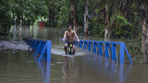 Sam Salvador rides his bike through floodwaters on the Ross River in the Townsville suburb of Mundingburra on Friday.
