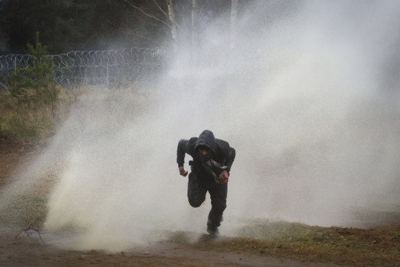 A man runs away from a water cannon during clashes between migrants and Polish border guards at the Belarus-Poland border on Tuesday.
