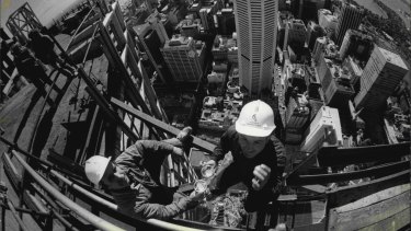 Cheers … A fisheye lens view from the top of Centrepoint tower as riggers, Mr Stan Kowalski of Randwick (left) and Mr Albert Fortini of Lidcombe, celebrate the tower’s rising past the MLC Centre.