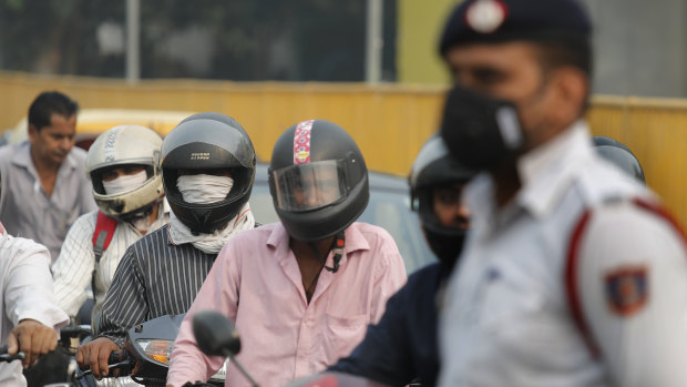 Motorcyclists cover their faces to save themselves from air pollution as they wait at a crossing in New Delhi, India.