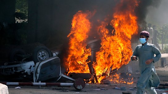 A man runs past a burning car set on fire by angry supporters of Pakistan’s former prime minister Imran Khan during a protest against his arrest, in Peshawar.