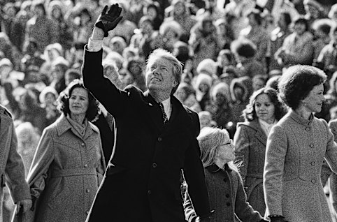 President Jimmy Carter waves to the crowd while walking with wife Rosalynn and their daughter, Amy, to the White House following his inauguration on January 20, 1977.