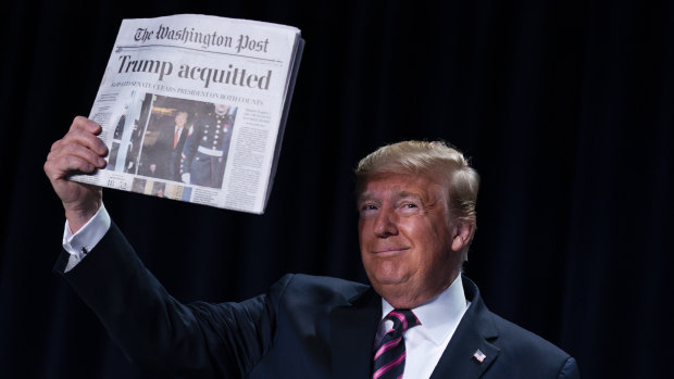 President Donald Trump holds up a copy of the Washington Post during the annual National Prayer Breakfast a day after the Senate voted not to remove him from office.