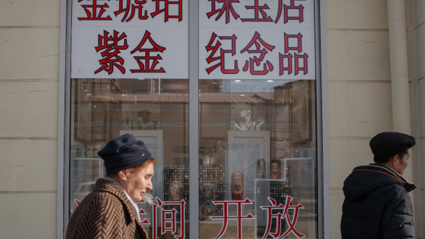 Pedestrians walk in front of a jewellery shop adorned with signs in Chinese, in Irkutsk, Russia