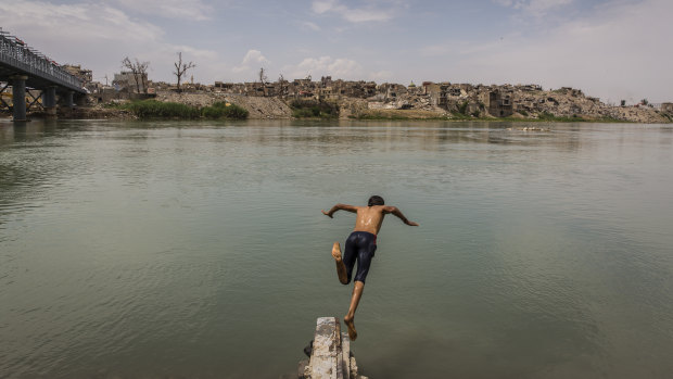A boy who had been collecting scrap metal cools off with a dip in the Tigris River, across from the destroyed Old City on the western side of Mosul.