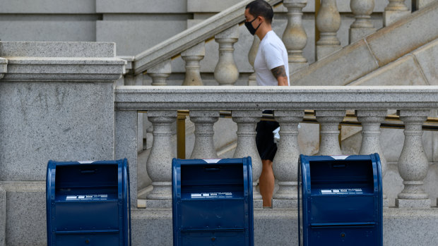 A person wearing a protective mask walks by United States Postal Service collection boxes near Capitol Hill in Washington, DC.