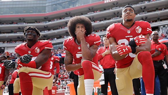 Iconic moment: Kaepernick, centre, takes a knee during the US national anthem in 2016.