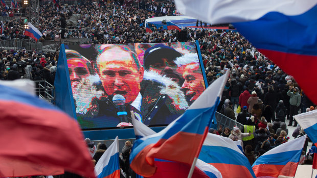 Attendees wave Russian flags in support of President Vladimir Putin as he speaks on screen during a pre-election rally at Luzhniki stadium in Moscow in March. 