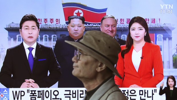 A man passes by a TV screen showing file footage of CIA Director Mike Pompeo, center right, and North Korean leader Kim Jong Un, centre left, during a news program.