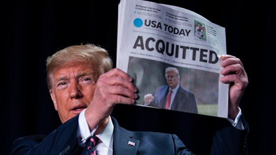 Donald Trump holds up a newspaper following his acquittal in the Senate.