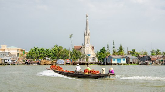 Barcos de madera tradicionales cruzan el Mekong con la iglesia de Cai Be al fondo.