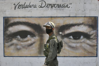 A soldier and the late Venezuelan president Hugo Chavez (mural) keep an eye on voters at a polling booth in Caracas.