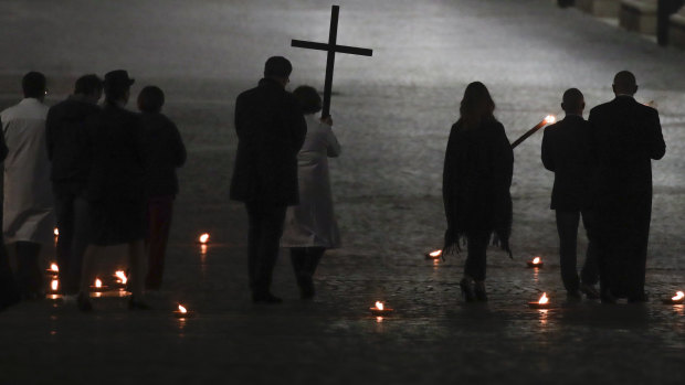 A woman holds the cross during the Via Crucis – or Way of the Cross – ceremony in a St Peter's Square empty of the faithful following Italy's ban on gatherings.