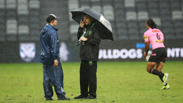 Ground staff speaks to an NRL official as they stand in heavy rain at Bankwest Stadium on Saturday afternoon.
