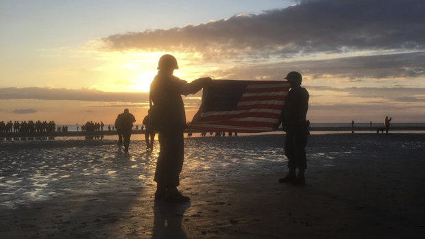 Re-enactors hold an American flag at sunrise as part of events to mark the 75th anniversary of D-Day on Omaha Beach.