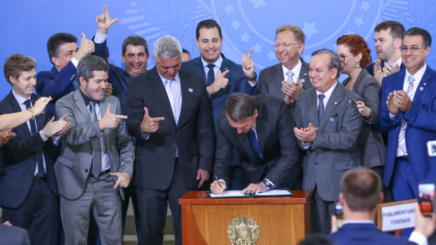 Brazilian President Jair Bolsonaro signs a decree easing gun laws in Brasilia while lawmakers celebrate.