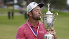 Jon Rahm, of Spain, kisses the champions trophy for photographers after the final round of the US Open Golf Championship. 