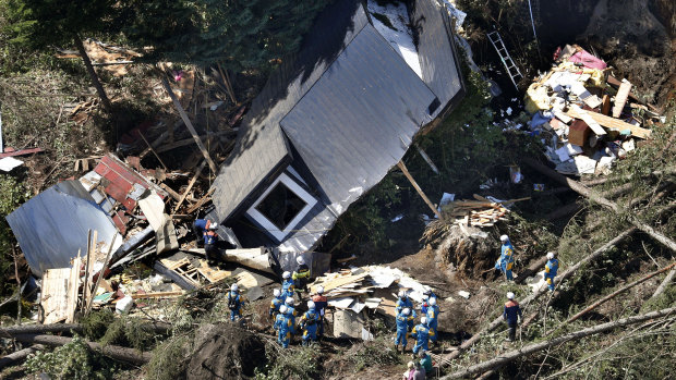 Police search for missing persons around houses destroyed by a landslide.