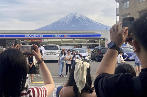 Visitors take photos of the view of Mount Fuji in front of a convenience store in Fujikawaguchiko. 