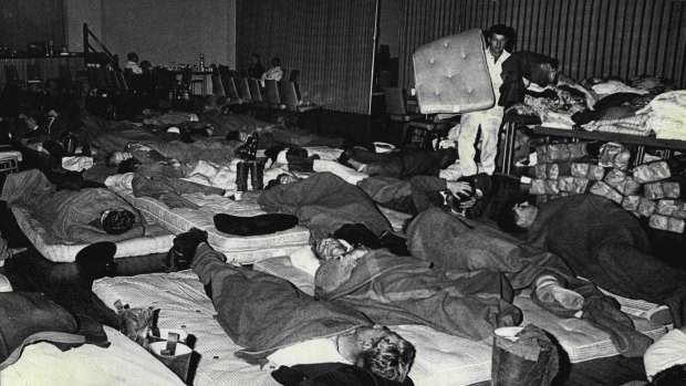 Weary after long hours battling the fires, firefighters stretch out on the floor of the Springwood Civic Centre with tired evacuees. November 30, 1968.