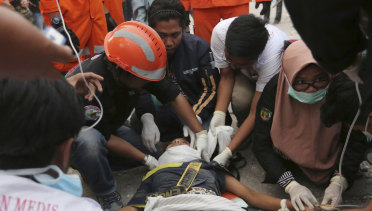 Rescuers check a survivor at restaurant building damaged by a massive earthquakes and tsunami in Palu.