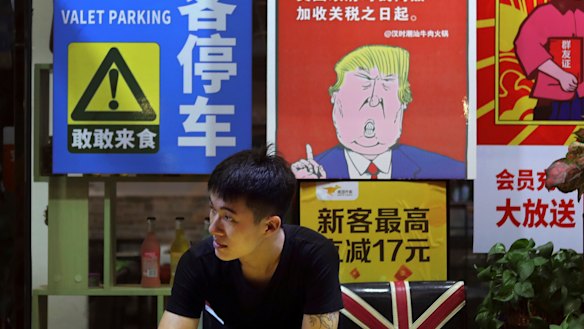 A man in Guangzhou stands near a poster depicting a mural of Donald Trump stating that all American costumers will be charged 25 per cent more than others starting from the day he started the trade war against China. 