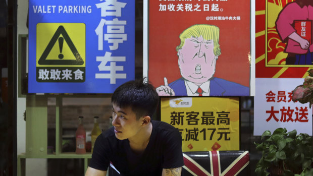 A man in Guangzhou stands near a poster depicting a mural of Donald Trump stating that all American costumers will be charged 25 per cent more than others starting from the day he started the trade war against China. 