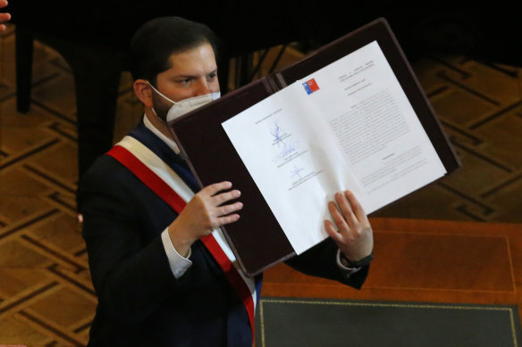 Chilean President Gabriel Boric holds up the final version of the country’s new constitution during a ceremony at the former Congress in Santiago.