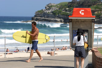 A surfer walks past a woman using a Telstra payphone on Sydney’s Bondi Beach. Payphones are still being used despite the prevalence of mobile phones.