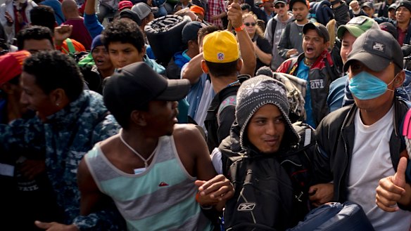 Migrants link arms as they march together with the intention of crossing the US border as a group at the Chaparral border crossing in Tijuana.