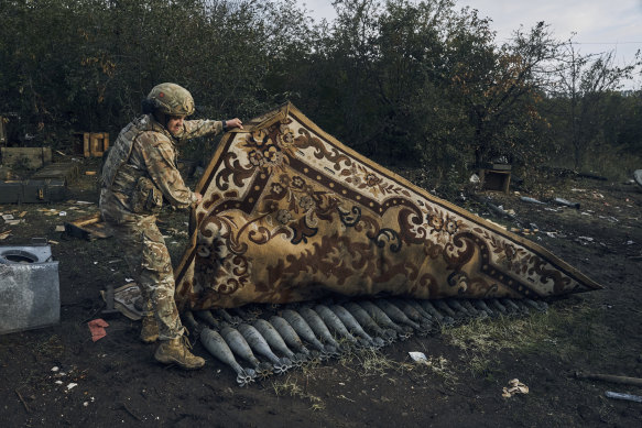 Ukraynalı bir asker İzyum'da Rus mühimmatını kaplayan halıyı kaldırıyor.