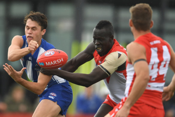 North Melbourne's Curtis Taylor gets a handball away despite the attention of Sydney's Aliir Aliir in Hobart during the pre-season.