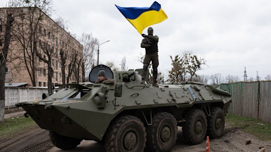 Ukrainian soldier waves Ukrainian national flag while standing on top of an armoured personnel carrier.