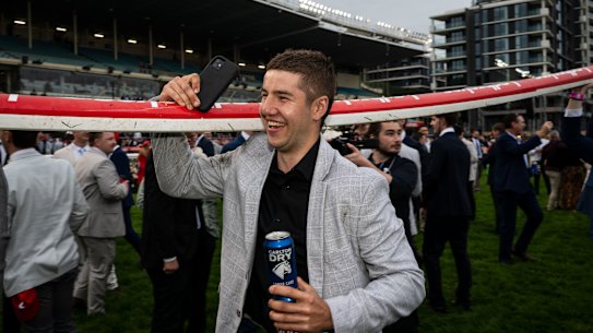 Phone in hand, rail over shoulder for this racing fan.