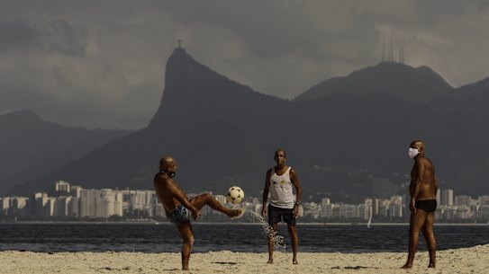 People play football on a Niteroi beach, with Rio de Janeiro and its Sugar Loaf in the background. Despite the proximity, the two cities have very different rates of dengue.