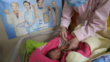A baby receives a vaccine shot next to a poster that reads 'Standardise vaccination and build a healthy China'.