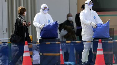 Officials in protective suits help a passenger disembarked from the quarantined Diamond Princess cruise ship anchored at a port in Yokohama, near Tokyo, Thursday, Feb. 20, 2020.