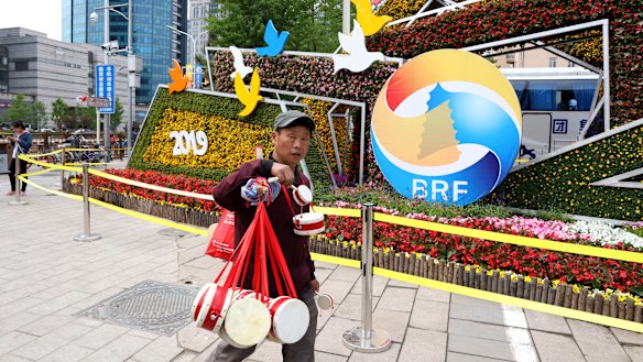 A man selling Chinese drums walks past a decoration promoting the upcoming Belt and Road Forum in Beijing.