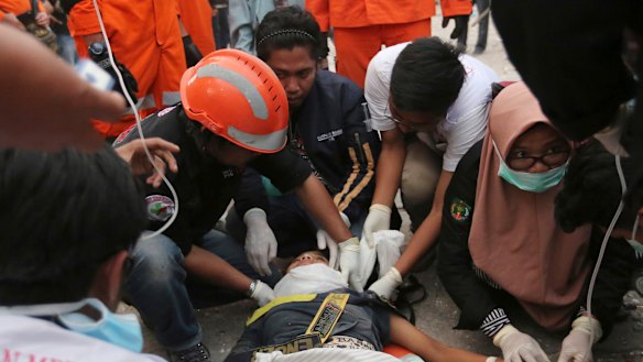 Rescuers check a survivor at a restaurant damaged by massive earthquakes and tsunami in Palu.
