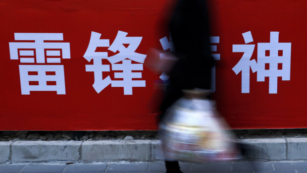 A woman carries her groceries past a Chinese propaganda board depicting "Lei Feng Spirit" on a pavement in Beijing on Tuesday.