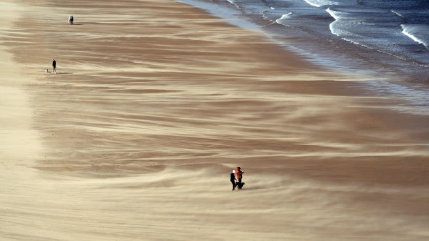 People walk along Tynemouth Beach on the North East Coast of England, as forecasters warn about strong storm winds across the region.