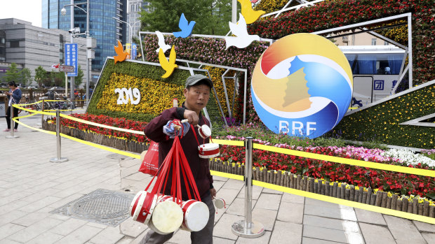A man selling Chinese drums walks past a decoration promoting the upcoming Belt and Road Forum in Beijing.
