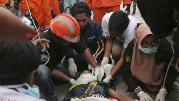 Rescuers check a survivor at a restaurant damaged by massive earthquakes and tsunami in Palu.