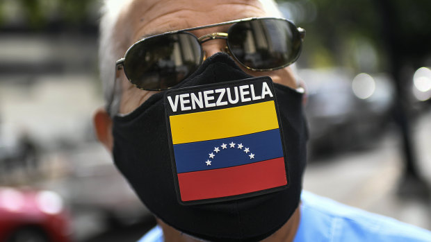 A man wears a face mask with the Venezuela flag, amid the spread of the new coronavirus, as he waits for hours to fill up his car at a state-run oil company PDVSA as station in Caracas.